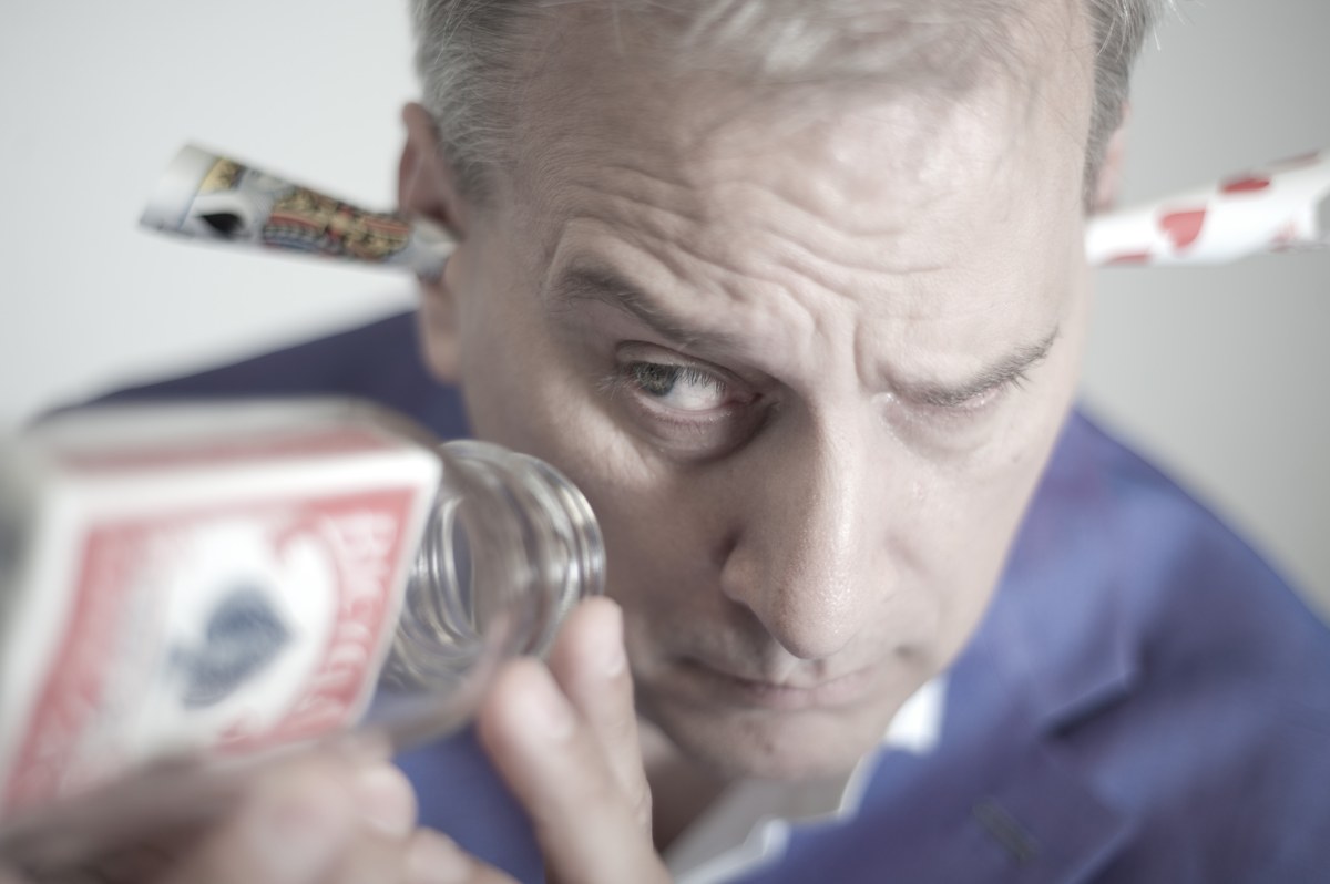 David Williamson peering at the camera with playing cards and a bottle