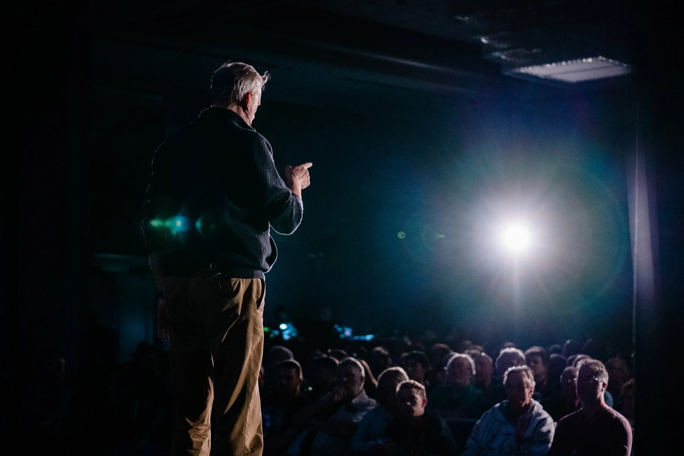 David Williamson teaches magic to a seated audience, viewed from the stage