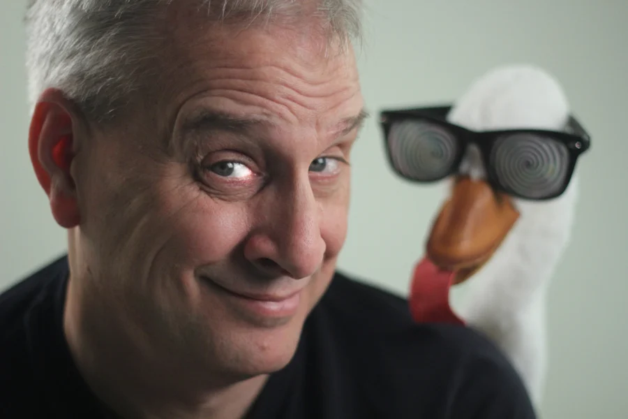 David Williamson beside his goose puppet wearing glasses