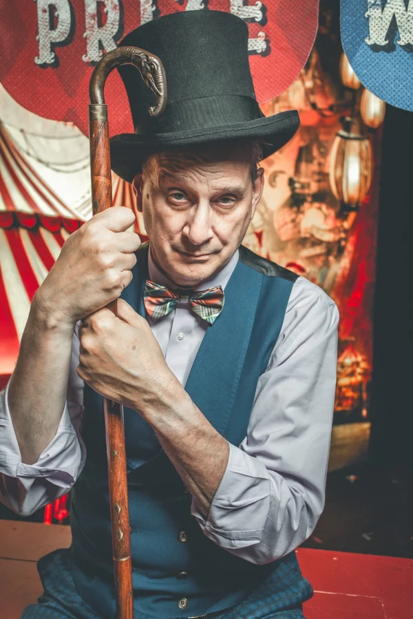 David Williamson in a top hat and ringmaster costume, leaning on a cane